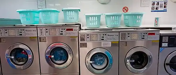 Primus washers with mint-green laundry baskets lined up on top, against white-tiled walls.