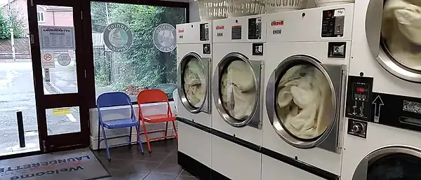Cissell dryers mid-cycle beside the doorway, with folding chairs and the branded welcome mat.