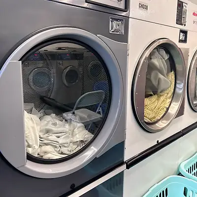 Row of industrial tumble dryers, the nearest door open with white laundry inside