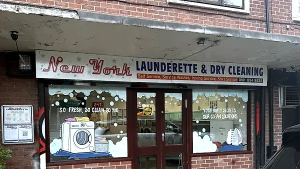 Painted New York Launderette & Dry Cleaning fascia above a brick shopfront with washing machine window art.